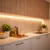 A spotless COB LED strip provides very warm white illumination under wooden kitchen cabinets, highlighting the backsplash and countertop.